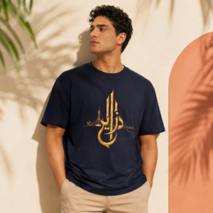 Mannequin homme portant un t-shirt bleu marine DZAYER avec calligraphie arabe dorée, mis en valeur dans une ambiance lifestyle premium Creamerch avec fond beige, lumière chaude et ombres végétales.